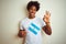 Afro american tourist man holding Argentinian Argentina flag over isolated white background doing ok sign with fingers, excellent