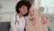 Afro american woman doctor and patient senior woman sitting on sofa and smiling