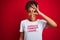 Afro american woman wearing funny t-shirt with irony comments over isolated red background with happy face smiling doing ok sign