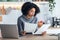 Afro business woman working with computer while consulting some invoices and documents in the kitchen at home