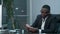 Afro businessman counting cash, sitting at desk in office