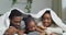 Afro family lying under blanket looking at camera showing like thumbs up noisy laughing having fun together at home