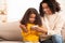 Afro Mother And Daughter Using Mobile Phone Sitting On Sofa