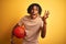 Afro sportsman with dreadlocks holding basketball ball over isolated yellow background very happy and excited, winner expression