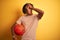 Afro sportsman with dreadlocks holding basketball ball over  yellow background stressed with hand on head, shocked with