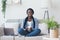 Afro woman freelancer sitting on couch with coffee and laptop