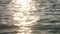 Afternoon or evening sun shines to calm sea, light reflecting on small waves, slow motion closeup detail