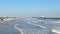 Afternoon ocean beach scene with sand, waves, cars, people and a tanker ship.