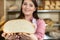 Against the backdrop of the bread shelves, a young attractive saleswoman shows a round cross-section of wheat bread