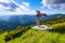 Against the background of beautiful mountain scenery with sun rays and cloudy sky the girl is staying in long dress, straw hat.