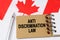 Against the background of the flag of Canada lies a notebook with the inscription - ANTI DISCRIMINATION LAW