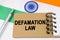 Against the background of the flag of India lies a notebook with the inscription - DEFAMATION LAW
