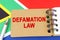 Against the background of the flag of South Africa lies a notebook with the inscription - DEFAMATION LAW