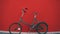 Against the background of a red wall, an old rusty green bicycle with flat tires