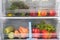 Against the background of a white refrigerator, the boxes contain vegetables and fruits, carrots, zucchini, bell peppers, apples,