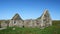 Against a clear blue sky on a sunny summer day, a static establishing long shot of an abandoned, derelict croft / farm house