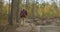 Aged fisherman is walking over coast of natural forest lake, carrying spin fishing rod, back view of man