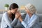 Aged grandmother adult granddaughter laughing seated on sofa enjoy talk