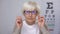 Aged lady putting eyeglasses on ad trying to focus vision, unhappy with result