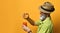 Aged male in hat, green shirt, sunglasses. He squeezes an orange into a glass of fresh juice, posing sideways on orange background