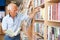 Aged man interested in books looking for necessary literature on shelves