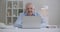 Aged man with moustache is working with laptop, sitting in room, answering at email, typing text of message, remotely