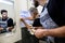 Aged plumber, repairman in uniform fixing electric boiler using flashlight while his young colleague helping him