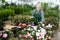 Aged saleswoman arranging potted blooming azaleas in garden shop