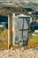 Aged and weathered metal trashcan with rusted over post and translucent plastic bag inside on trail or hiking park
