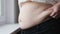 Aged woman compresses skin on abdomen checking fat excess