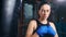 Aggressive female kickboxer with drops of sweat on face in blue wrapped hands posing at dark gym