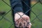 Aggressive  teenage boy showing hes fist behind wired fence at the correctional institute, the word hate is written on hes hand