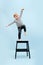 Agile blond boy balancing on one foot on a stepping stool. Over blue background
