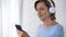 Aging lady in headphones holding mobile phone scrolling screen, choosing song