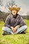 Aging man resting on sunny park grass in dark shirt and hat