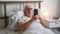 Aging senior man male in bed at home flat, tired sick ill alone retired and resting virus taking care unhappy sad, hold smartphone