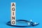 Aging word written on wooden blocks and stethoscope on light blue background