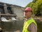 An aging worker in a helmet against the backdrop of hydroelectric turbines