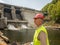 An aging worker in a helmet against the backdrop of hydroelectric turbines