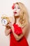 Agitated beautiful funny young blond pinup pretty woman with alarm-clock in red dress wonderingly looking at camera