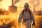 Agricultural care man in protective gear fumigates field at sunset