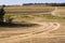 Agricultural fields empty after harvesting, winding countryside dirt road with tyre tracks in dust during a drought