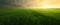 Agricultural green field in the evening, countryside landscape lit by dramatic sunset. Realistic generative AI illustration