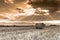 Agricultural landscape image, round hay bales on field, vibrant orange sky with divine lights