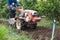 Agriculturist controlling hand tractor plowing on soil field in plantation. Agribusiness preparing cultivated land for sowing