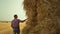 Agronomist checking hay bales at rural field. Focused farmer inspecting wheat