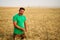 Agronomist examining cereal crop before harvesting sitting in golden field. Smiling farmer holding a bunch of ripe