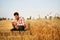 Agronomist examining cereal crop before harvesting sitting in golden field. Smiling farmer holding a bunch of ripe