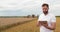 An agronomist stands with a tablet in a wheat field, a combine works in the background. A combine harvester harvests