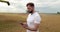 An agronomist stands with a tablet in a wheat field, a combine works in the background. A combine harvester harvests